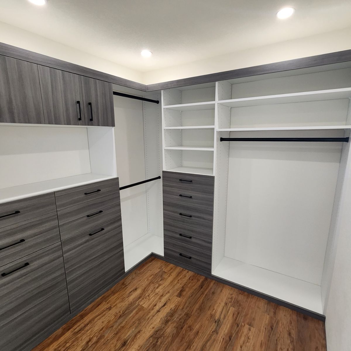Walk-in closet with grey and white shelving, drawers, and wooden floor.
