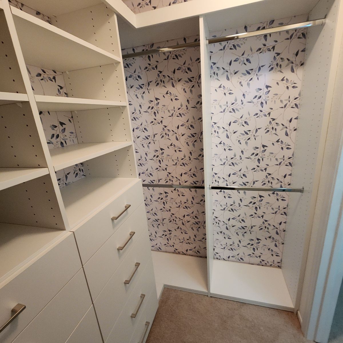 White closet with shelves, drawers, and hanging rods; walls have a blue leaf pattern.