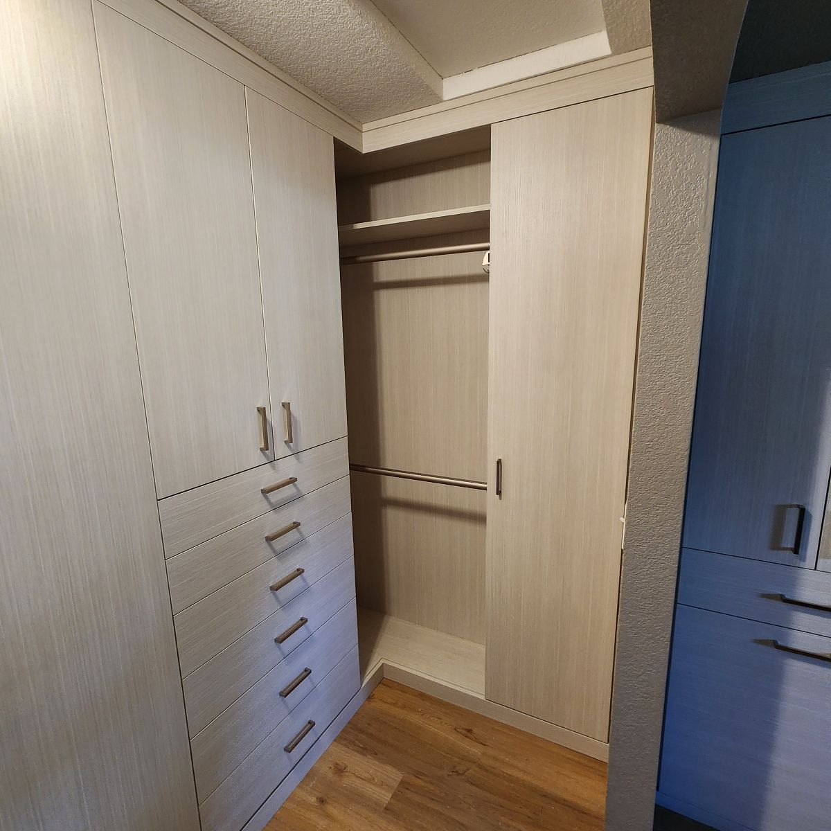 Built-in Walk in closet with light wood doors and drawers; one section open showing a hanging rod and shelf.