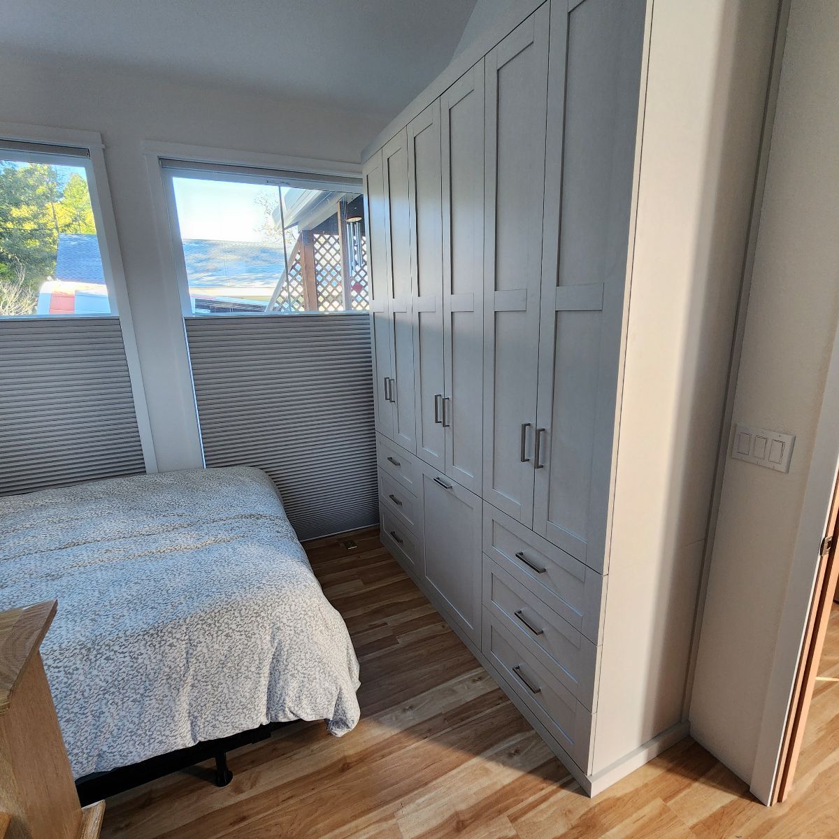 Bedroom with a large white cabinet unit. Bed is to the left, window is behind it.