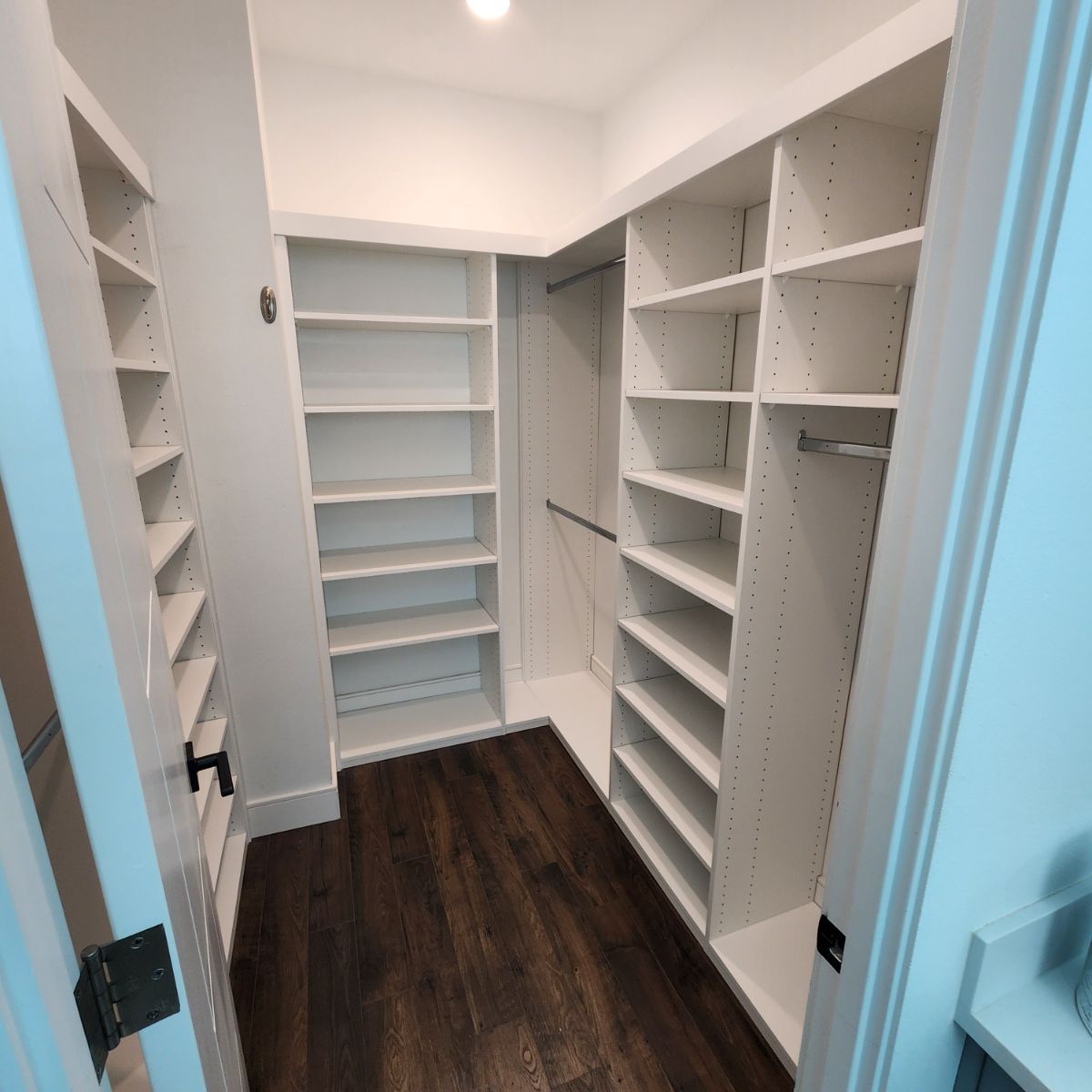 A walk in closet with lots of shelves and a wooden floor.