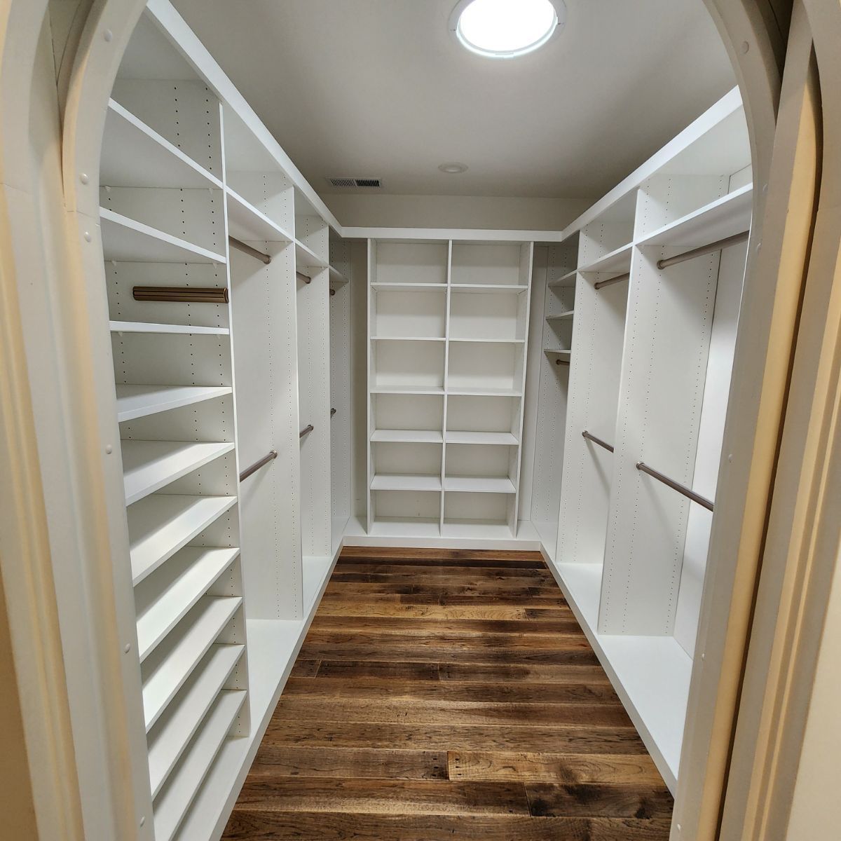 A walk in closet with white shelves and wooden floors
