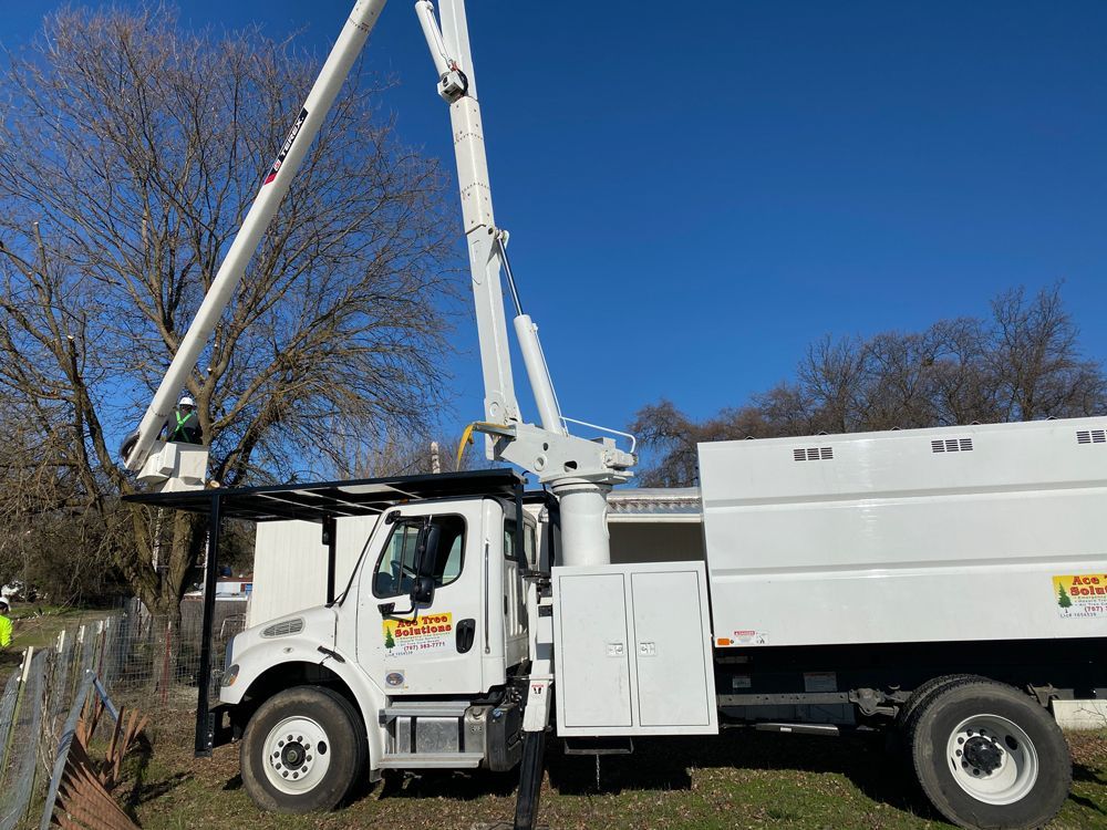 A white truck with a crane on top of it is parked in a field.