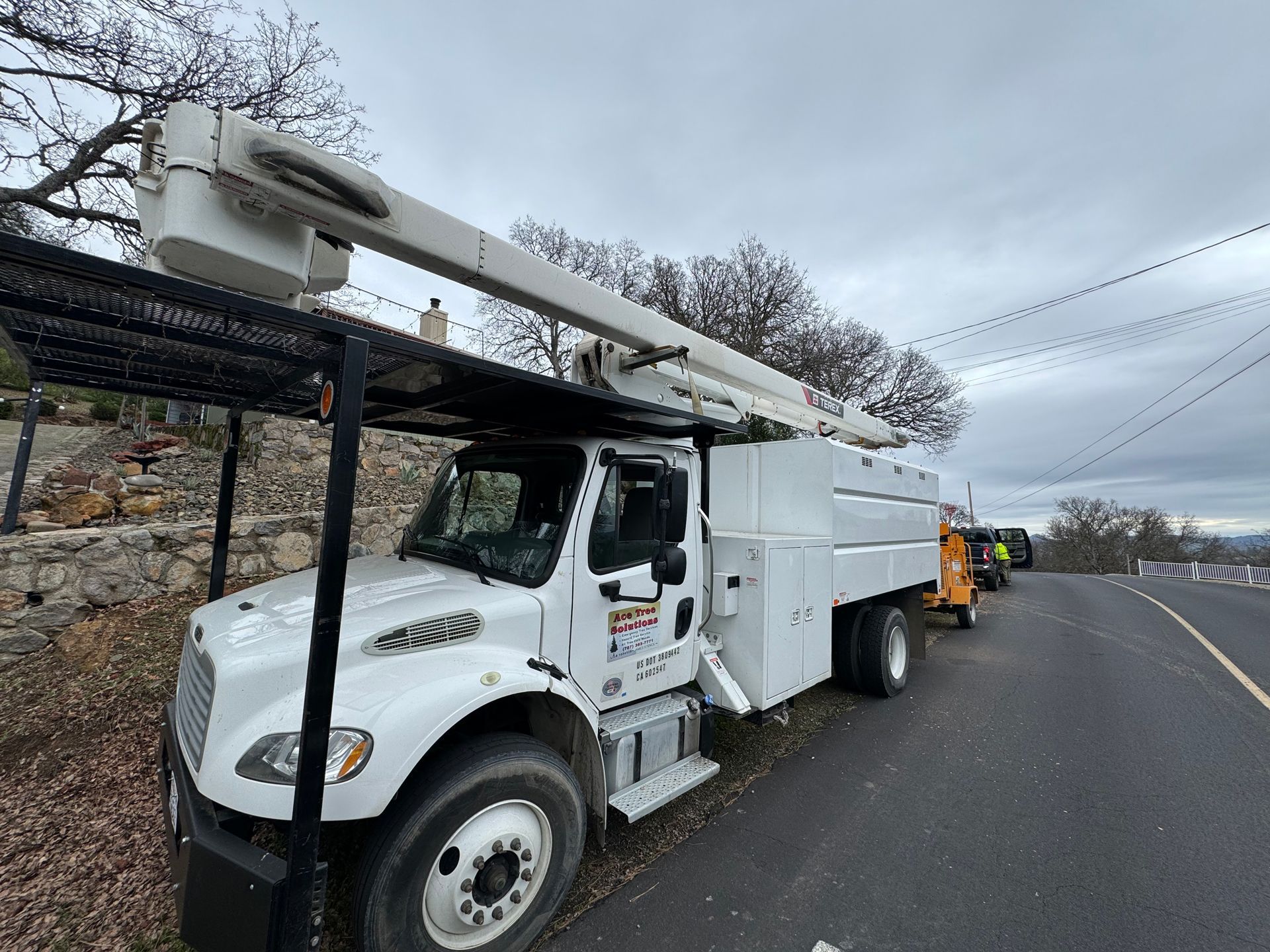 A white truck with a crane on top of it is parked on the side of the road.
