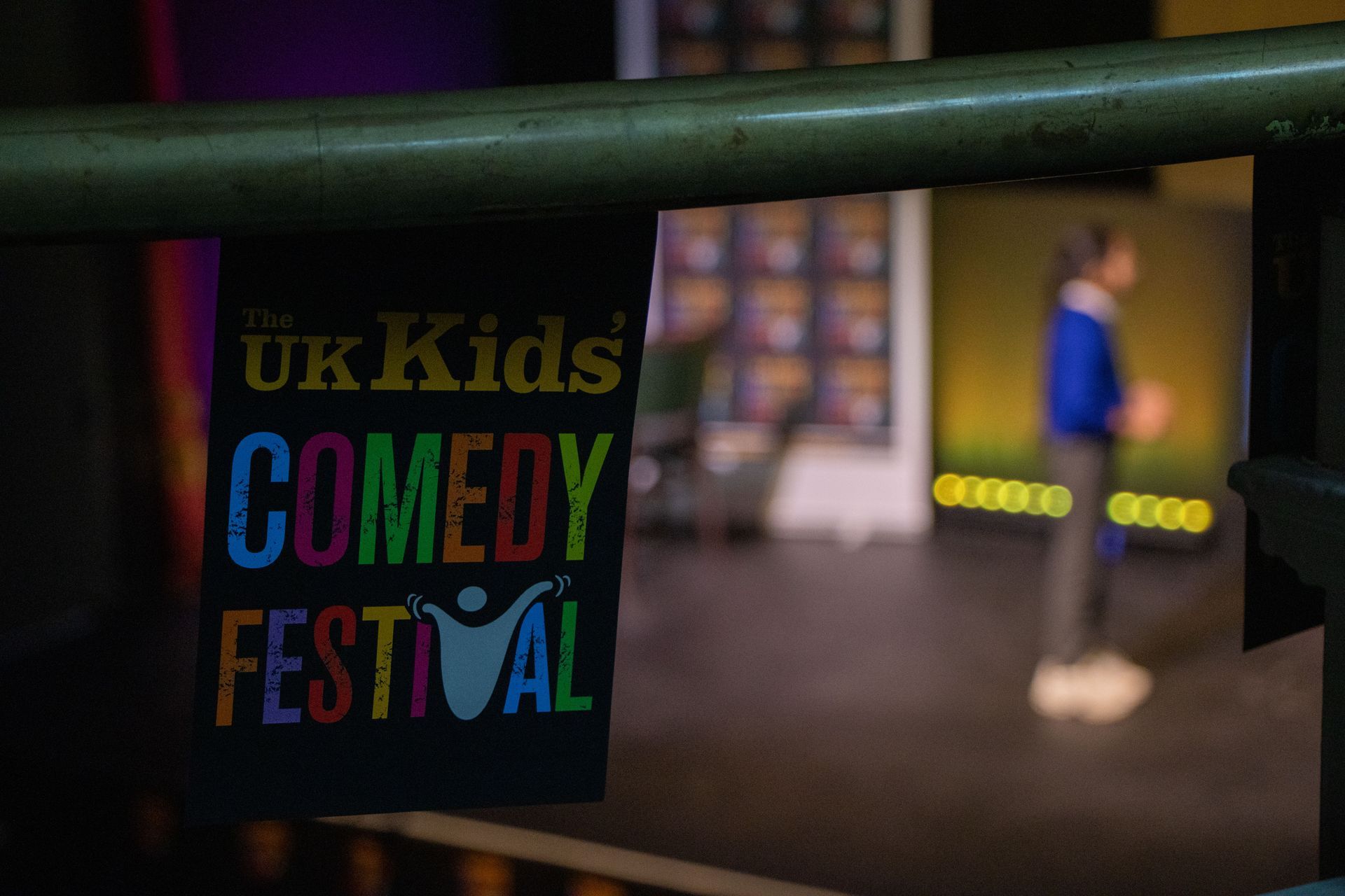 Two people on a stage with a presentation screen and banner. The setting is a theater.