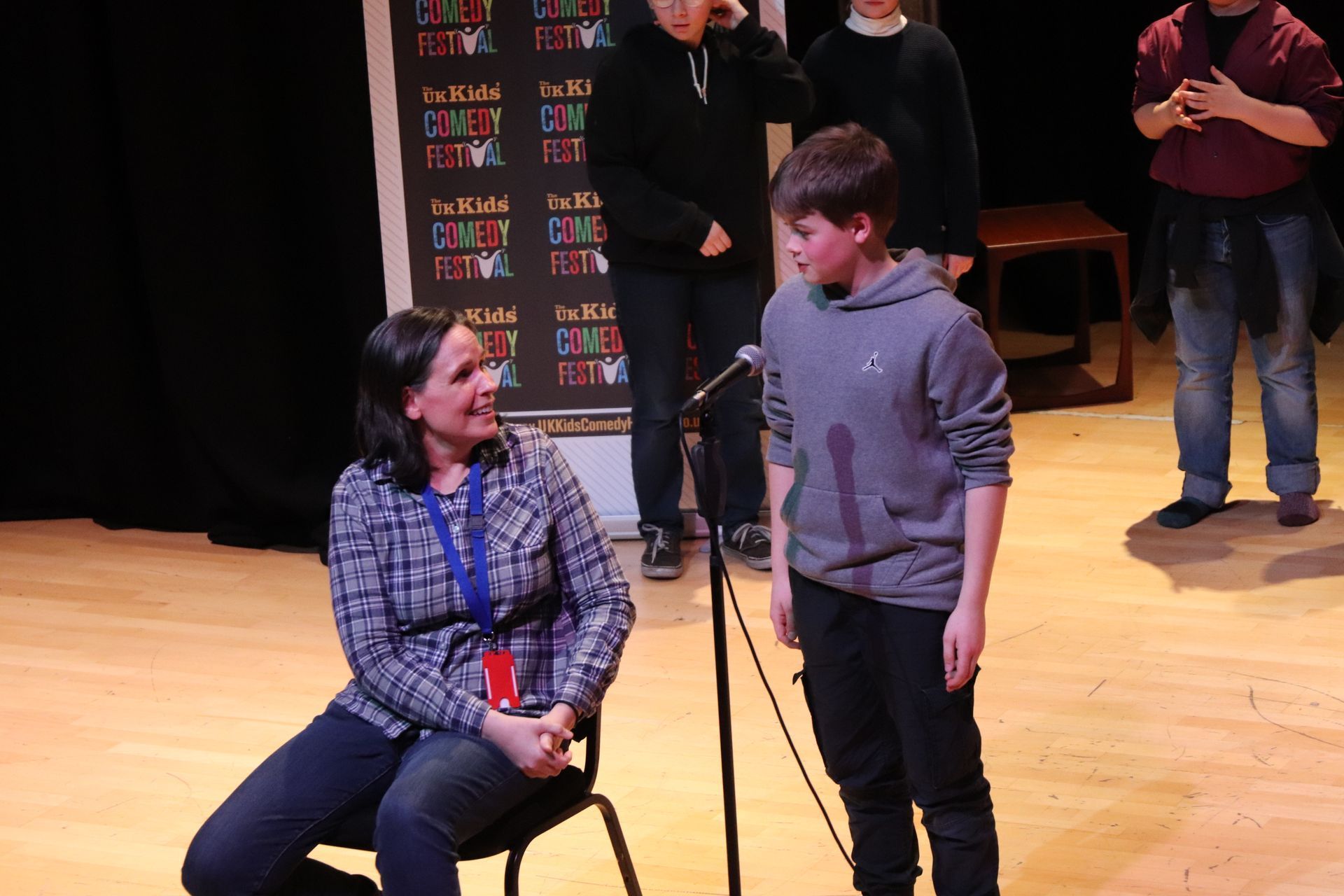 A woman and boy on a stage with a microphone. The boy is talking. Others stand behind them.