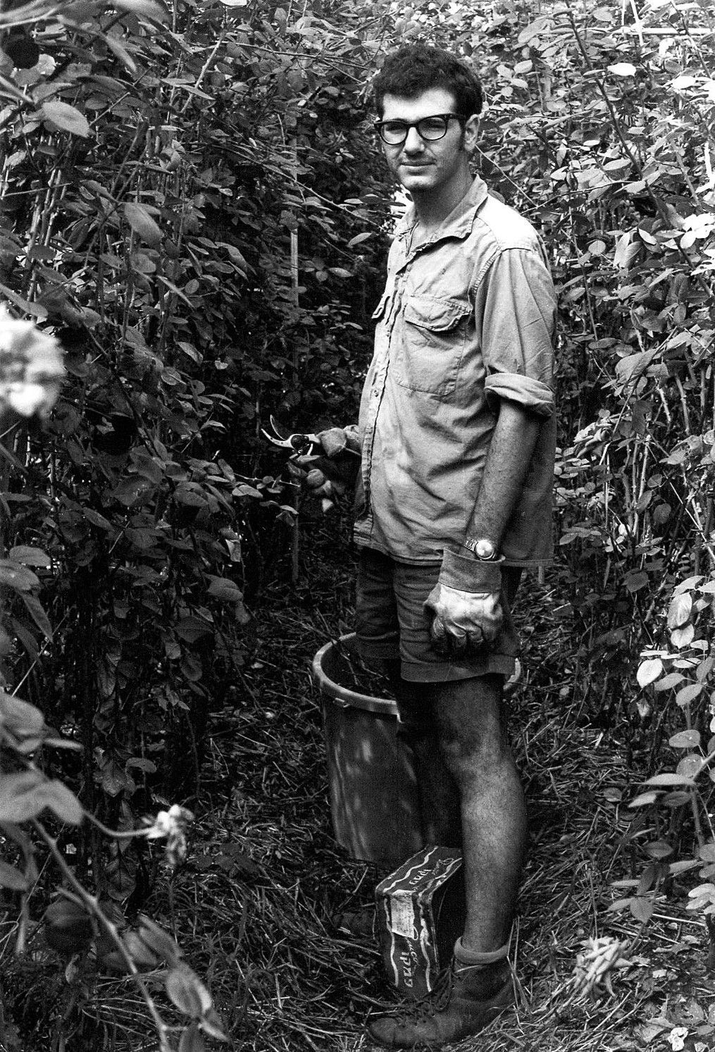 A man is standing in a field of plants holding a bucket. aliyah holds no allure for me