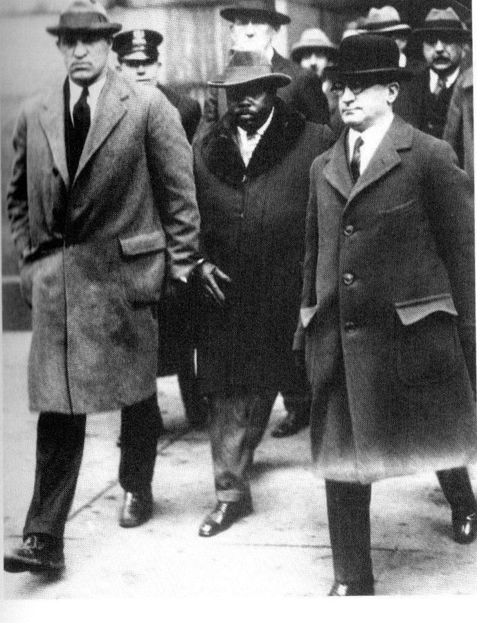 A group of men in suits and hats are walking down a street.