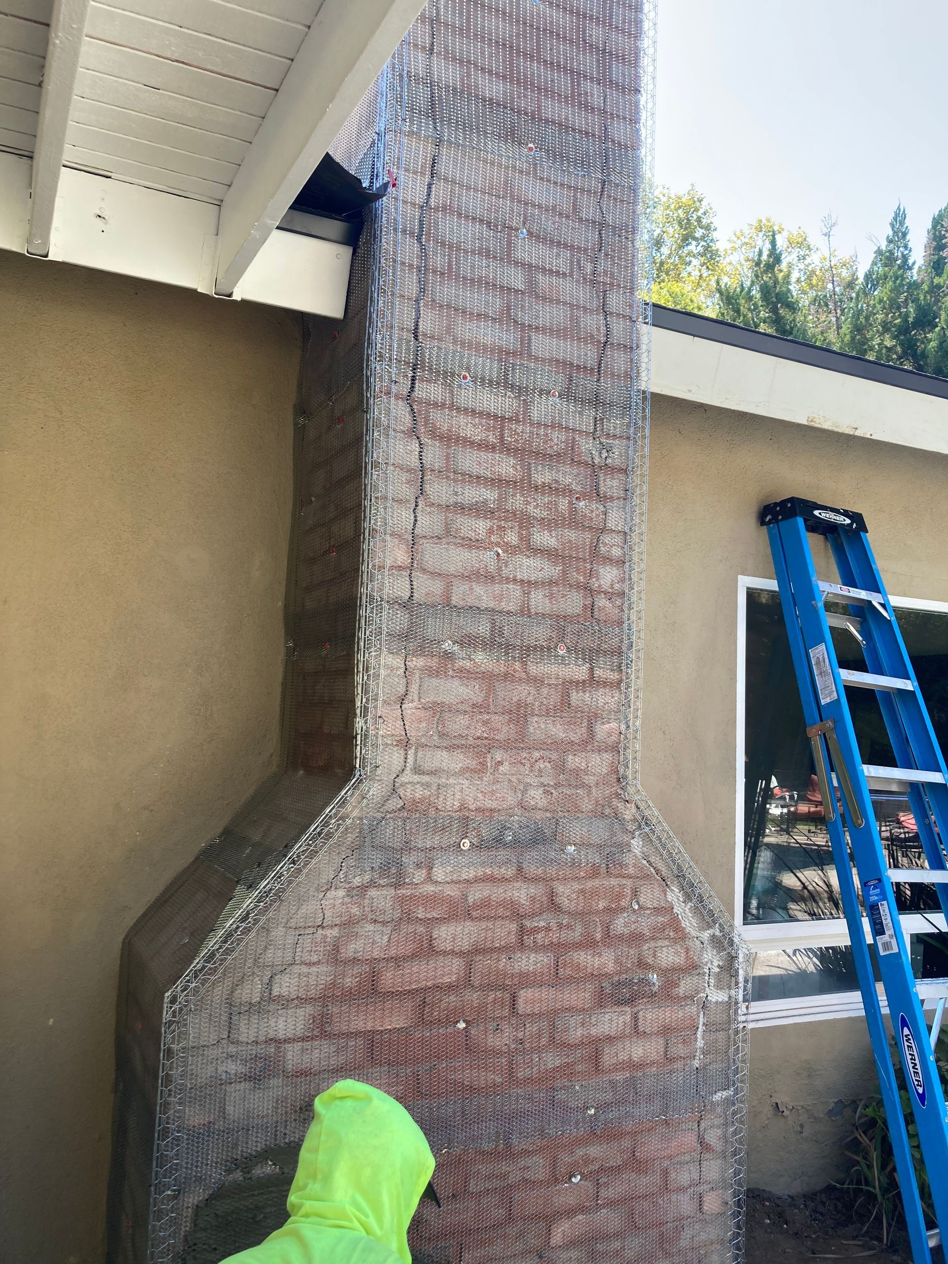 A man in a yellow jacket is working on a brick chimney.