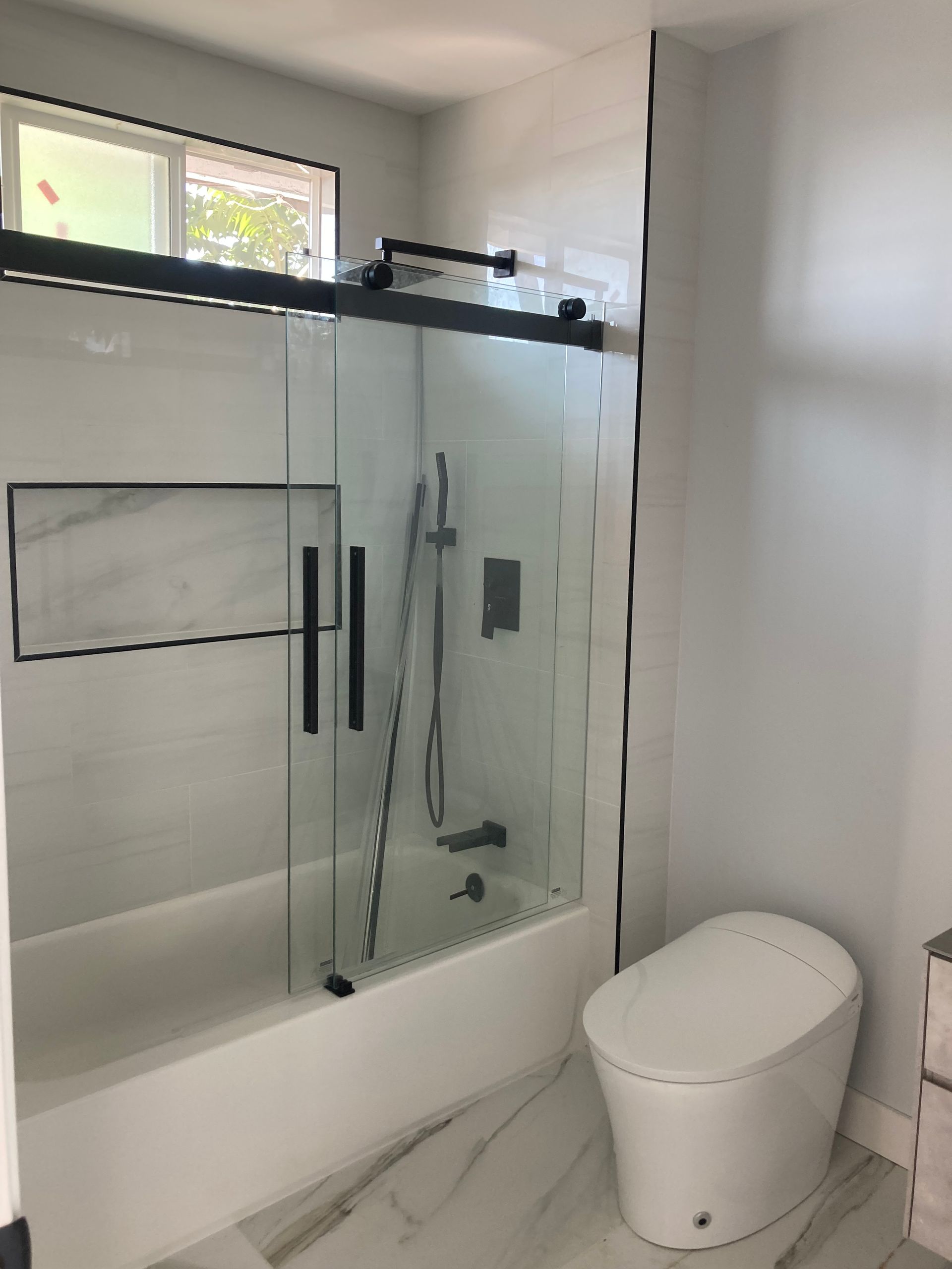 A bathroom with a toilet , tub , shower and window.