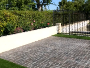 A brick driveway with a fence and a white wall in the background.