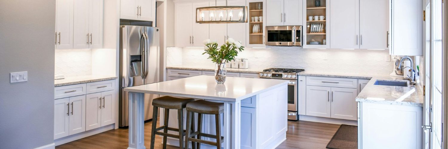 A kitchen with white cabinets , stainless steel appliances , and a large island.