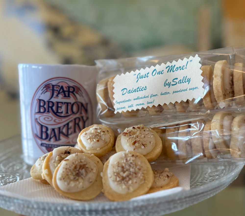 A glass plate topped with cookies next to a mug that says far breton bakery