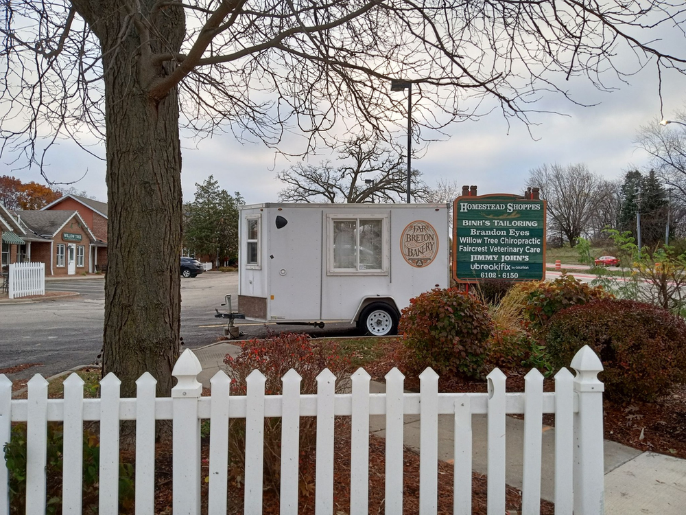 A white trailer is parked in front of a white picket fence