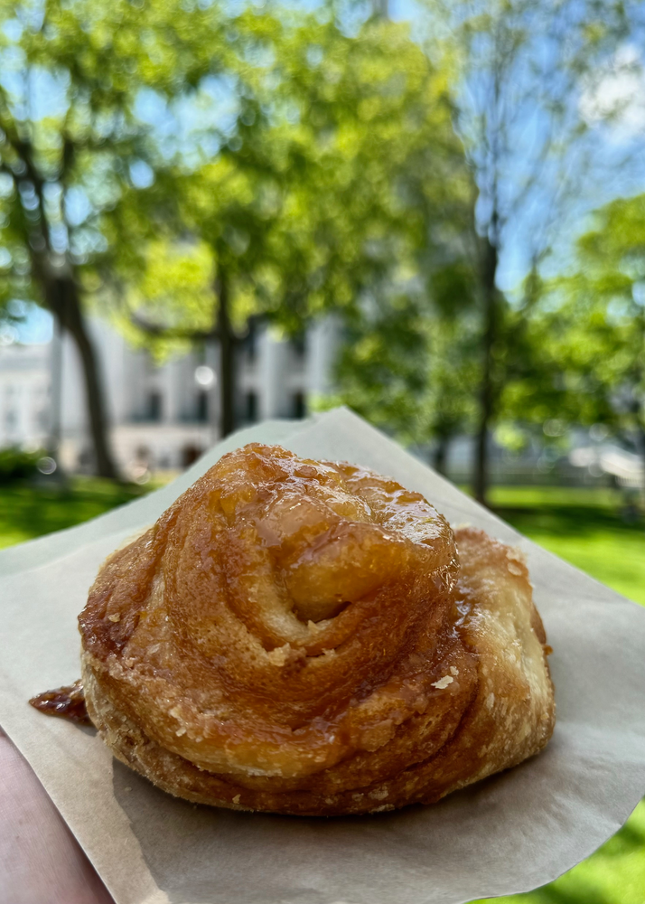 A person is holding a pastry on a napkin in front of a park.