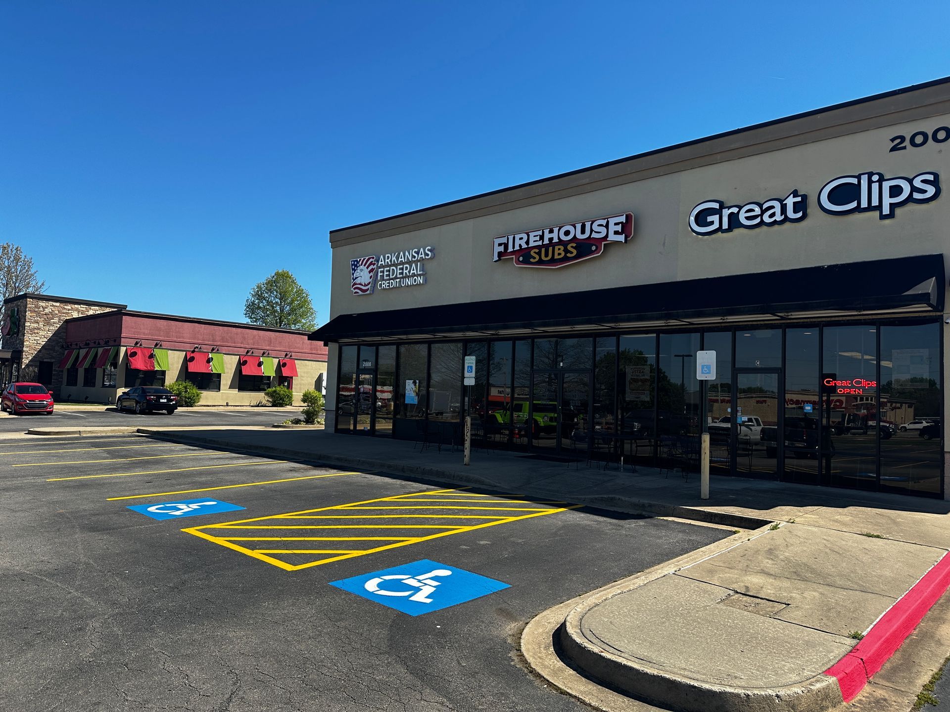 Exterior view of a shopping center with Firehouse Subs and Great Clips, blue sky, and accessible parking spaces.