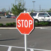 Black line painting machine applying a fresh stripe on a paved surface. Sunny outdoor setting.