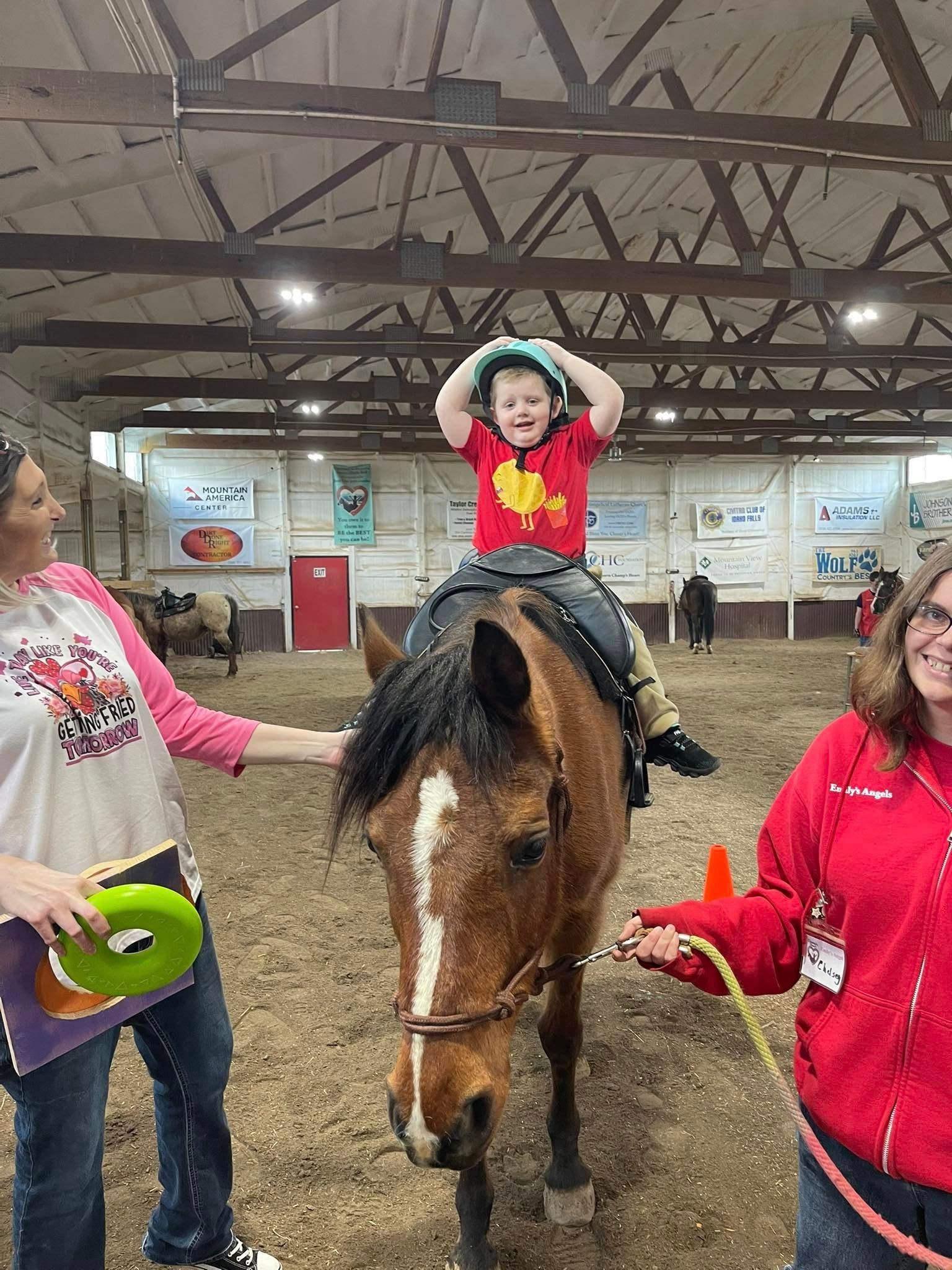 Child on horse, smiling, indoors. Two adults flank horse, smiling. Barn setting.