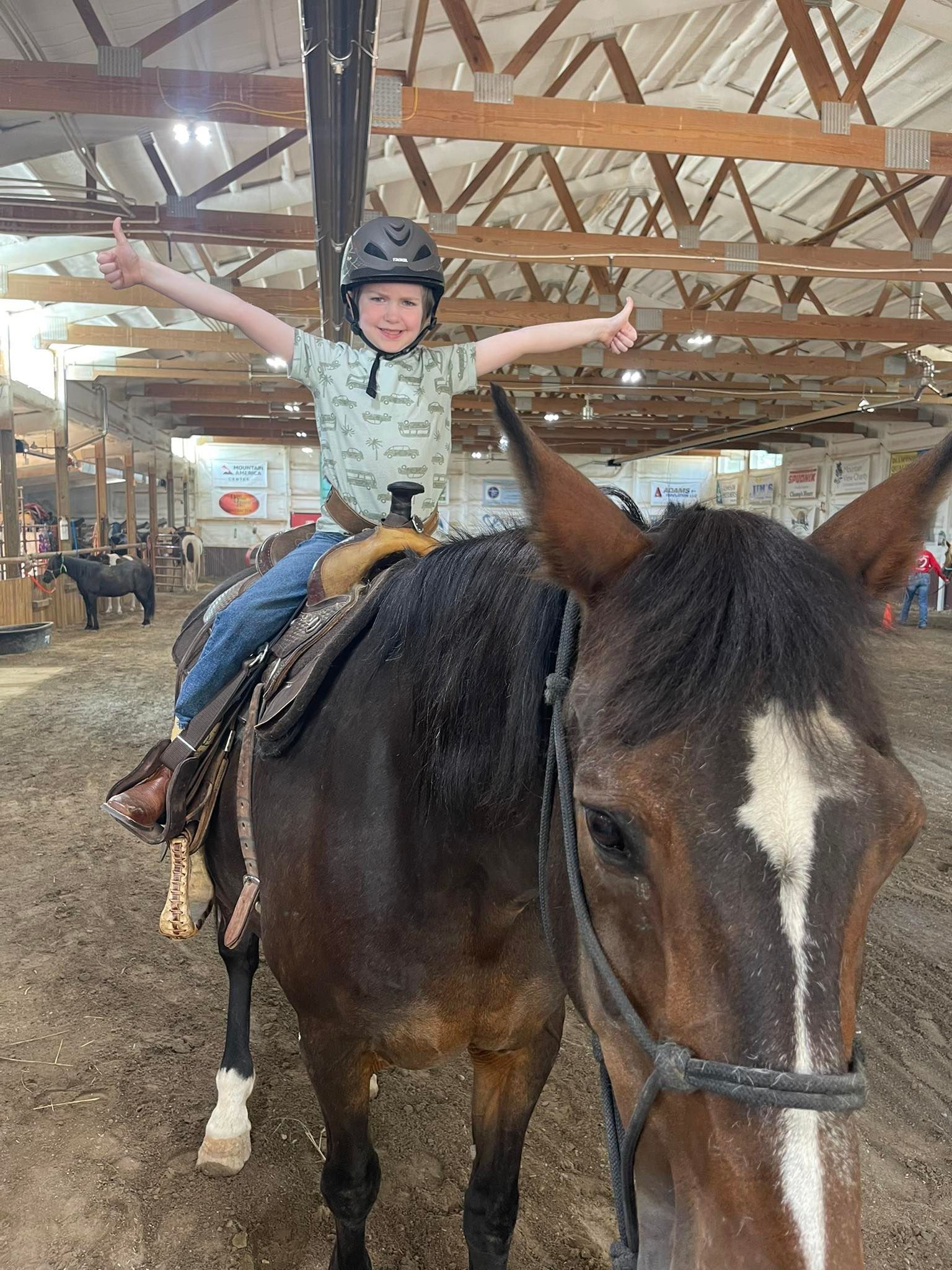 Boy on horseback with thumbs up in a stable.