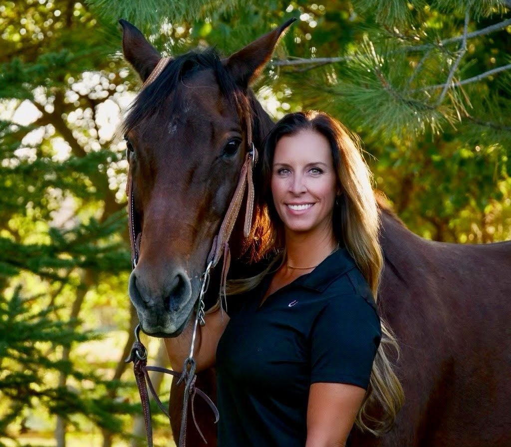 Woman smiles next to brown horse outdoors; they appear to be posing, and she is holding the horse’s bridle.