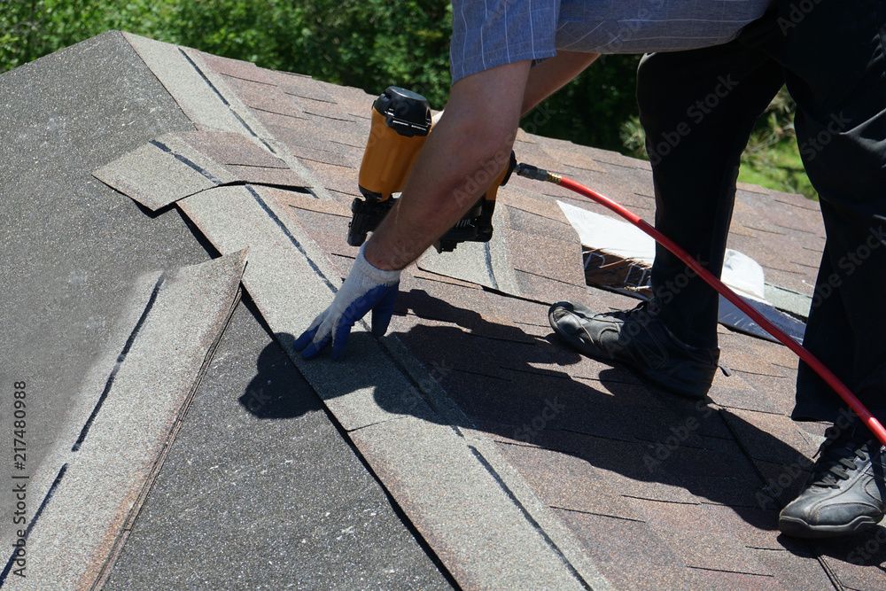 Roofer using a nail gun to install asphalt shingles on a roof.