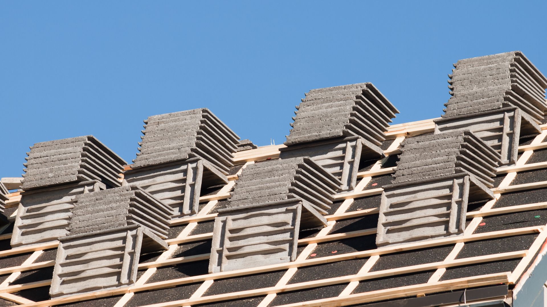 Roof under construction; stacks of gray tiles on wooden framework against a blue sky.