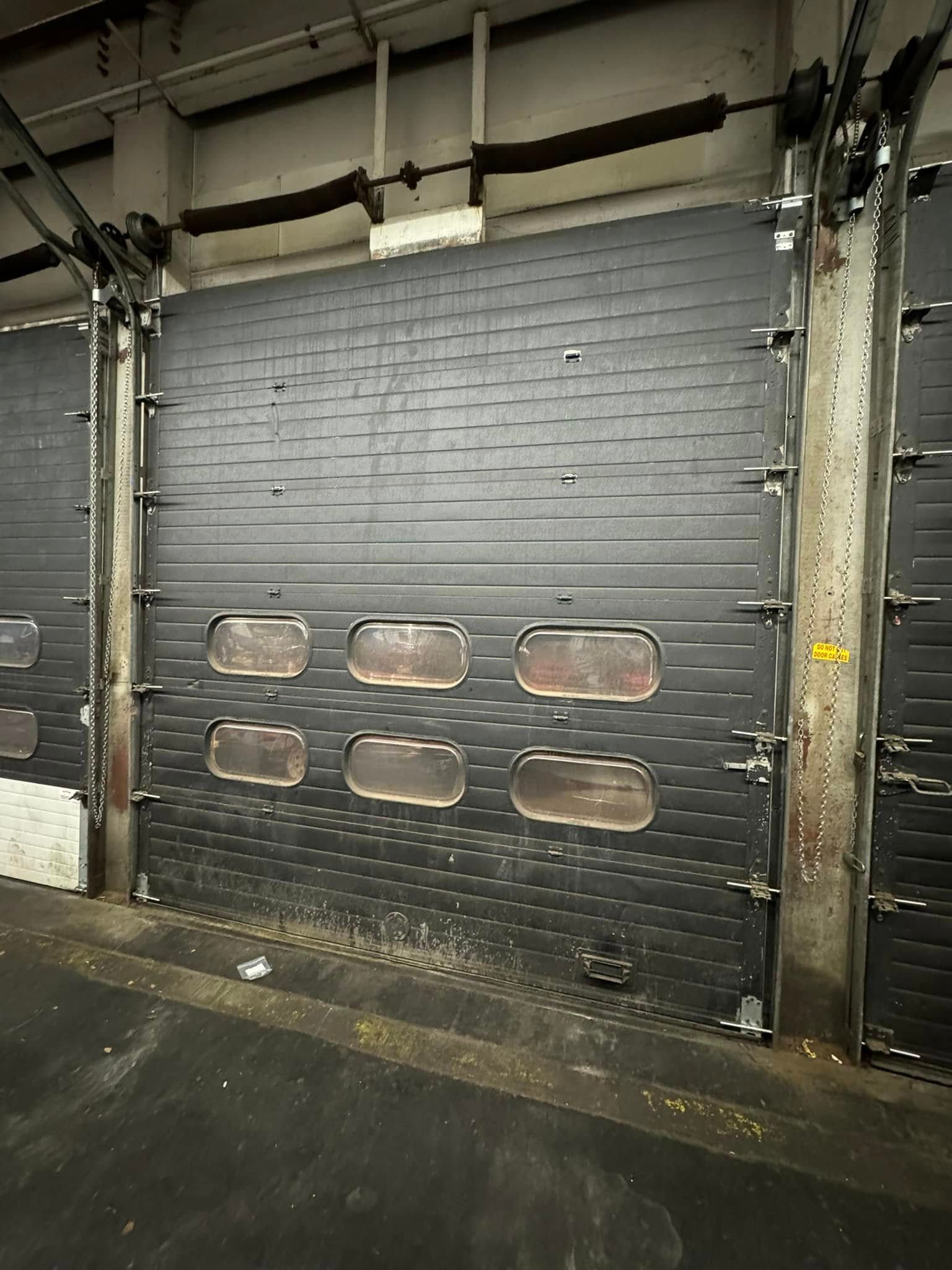 A dark gray overhead garage door with six rectangular windows, in an industrial setting.