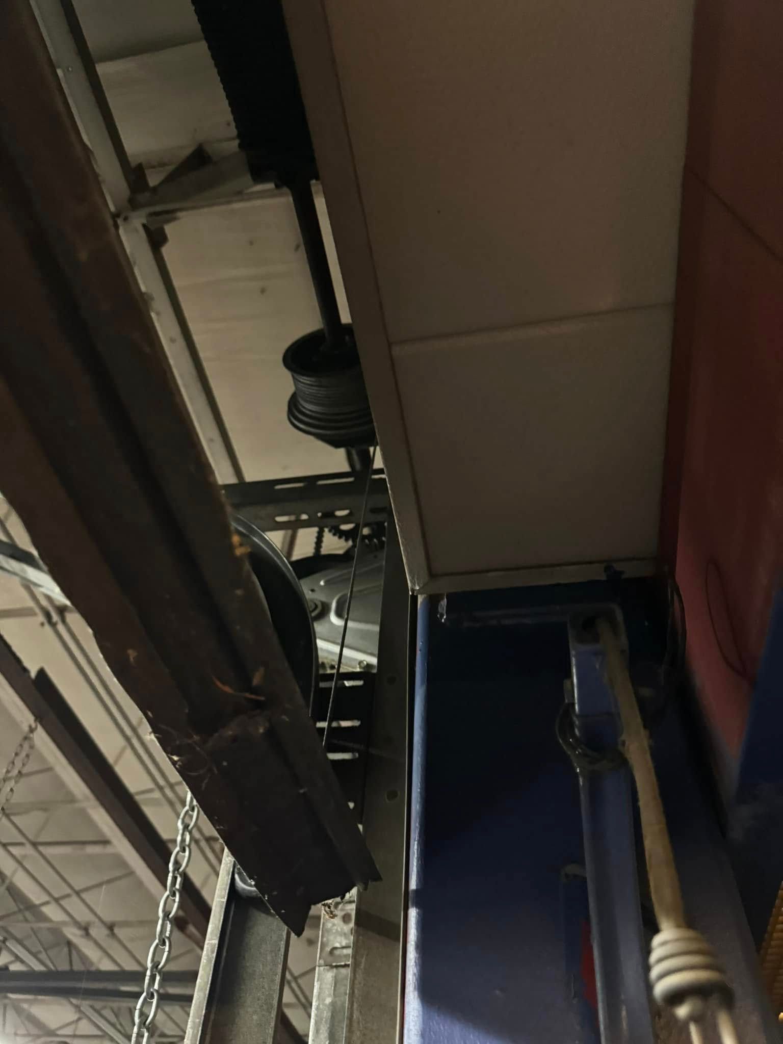 Overhead industrial mechanism with pulleys and metal beams, against blue and red walls.