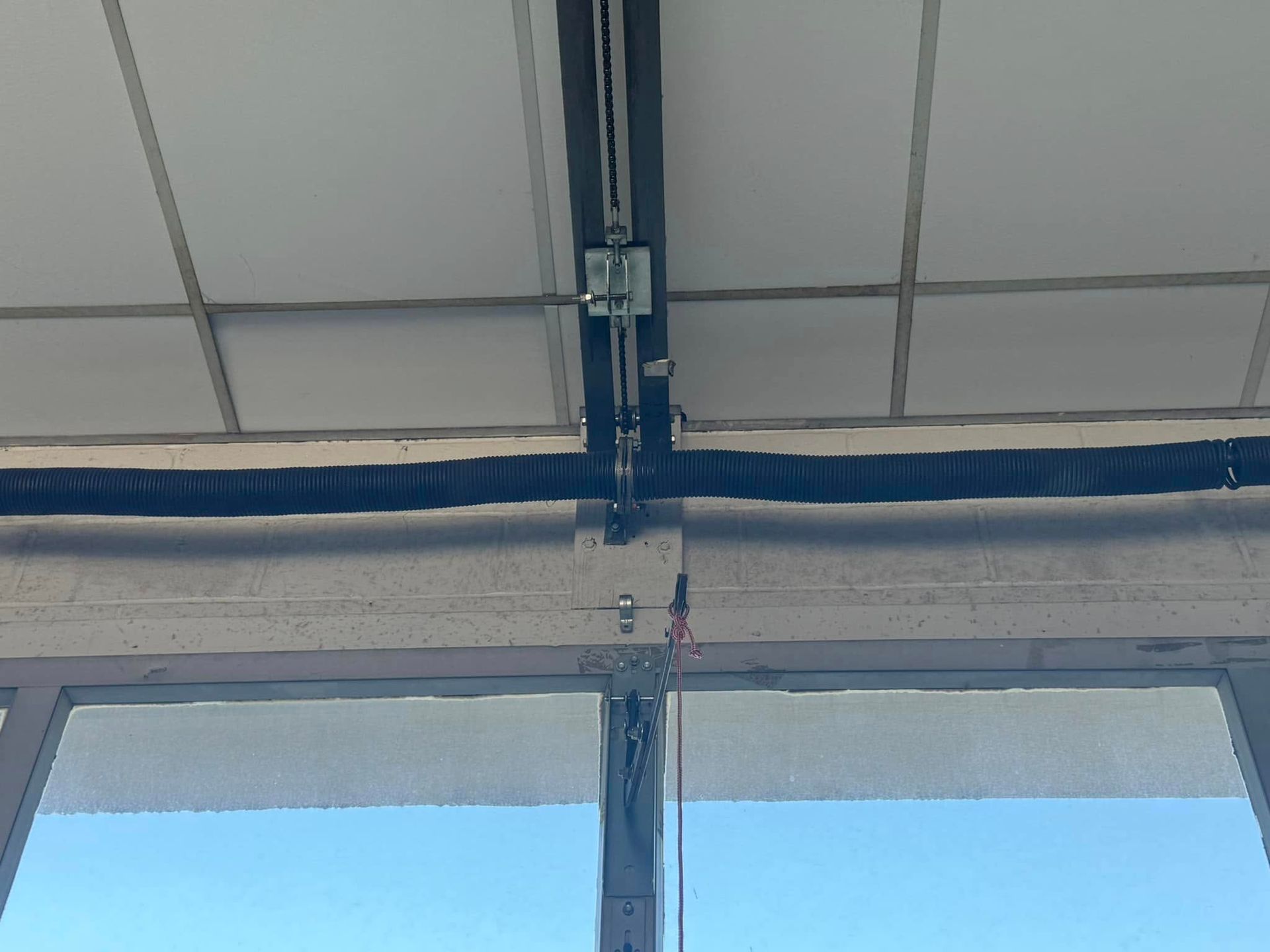 Ceiling with electrical conduits and wiring above a window with a blue sky view.