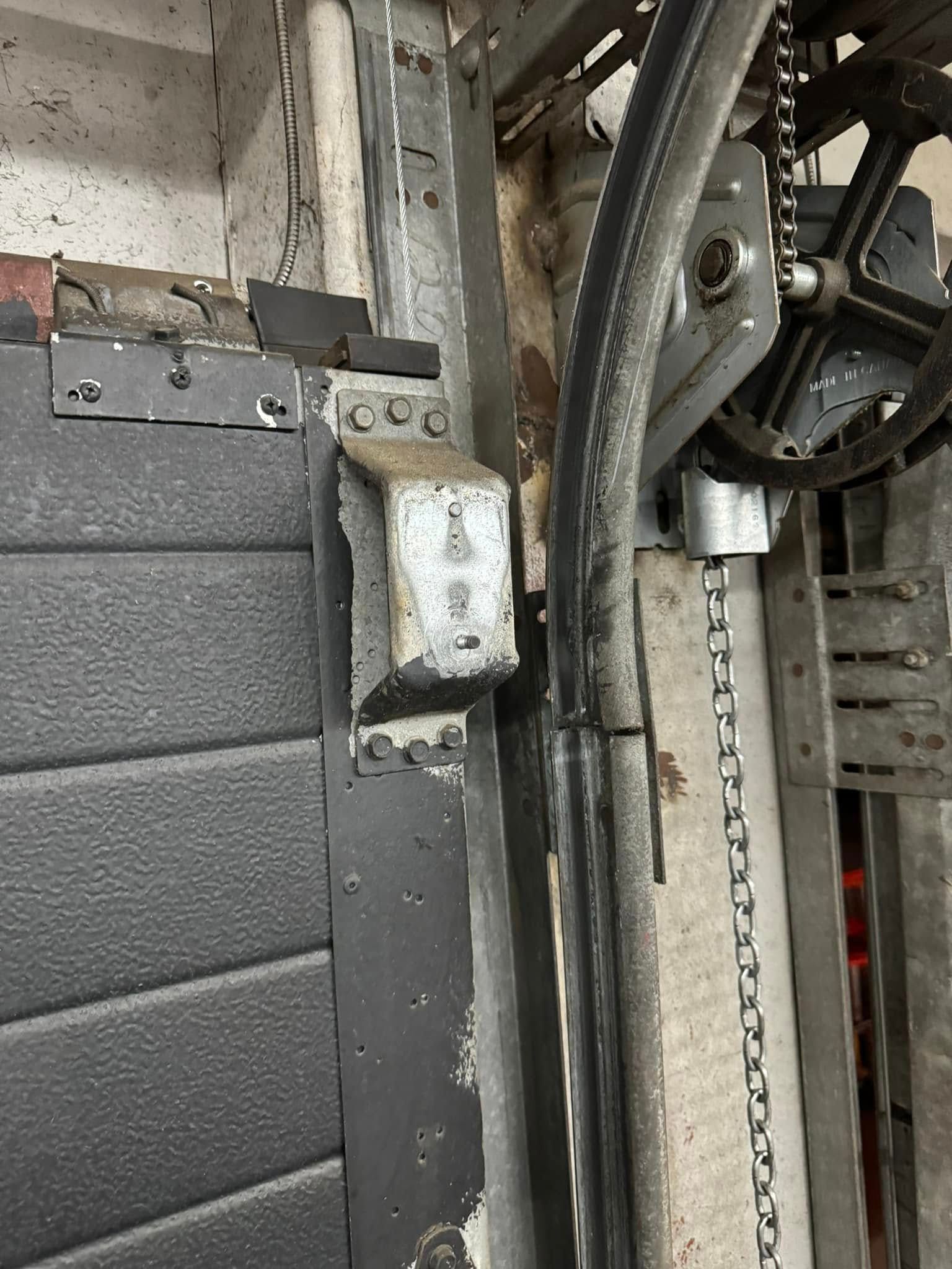 Garage door components: gray metal track, black door panel, chain, and motor.