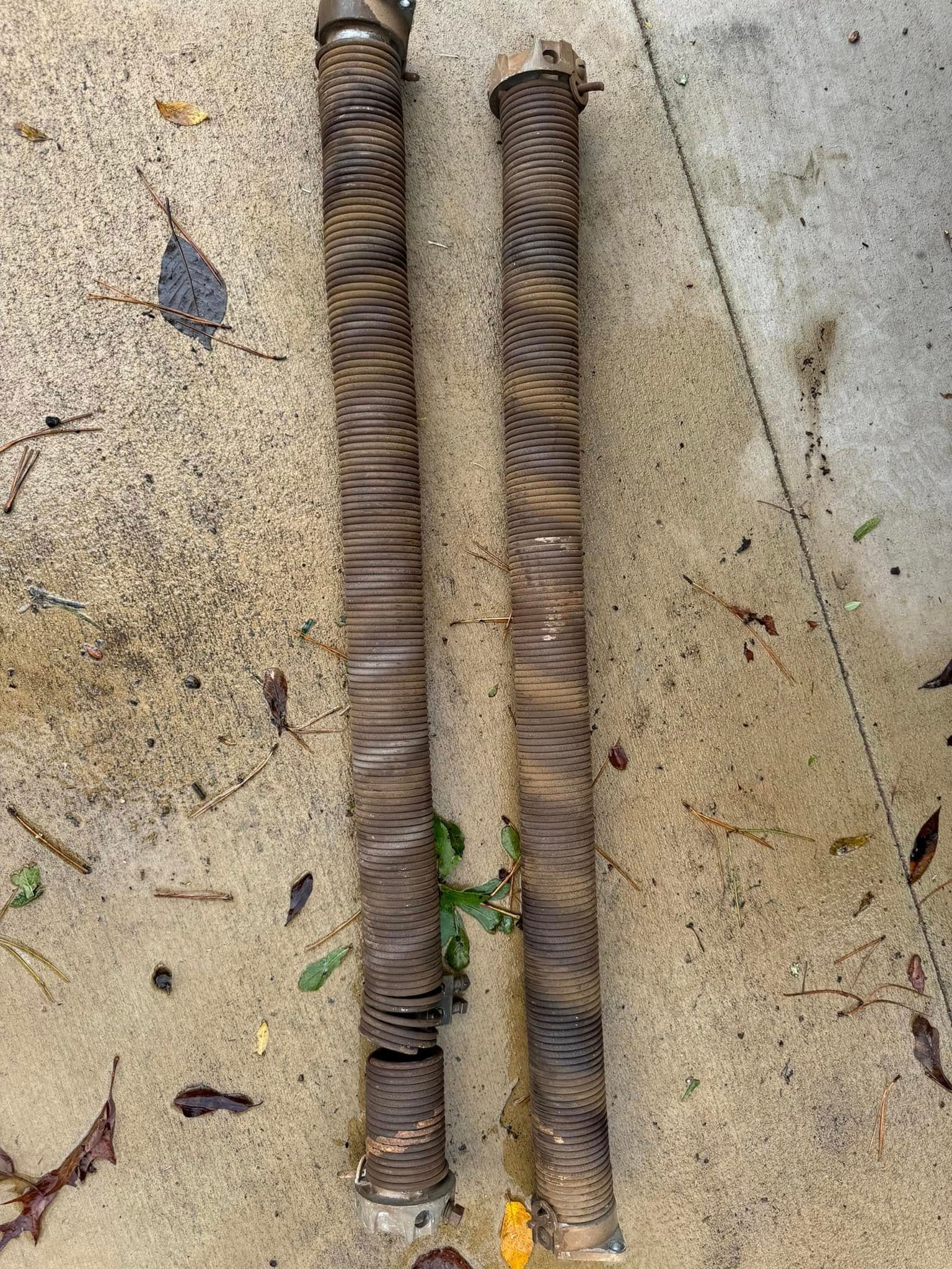 Two long, rusty springs laying on a concrete surface.