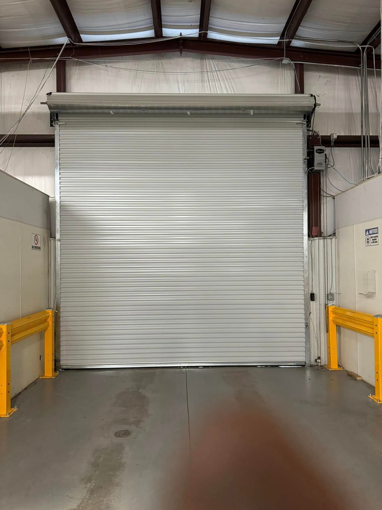 Closed, gray metal roll-up door in a warehouse, with yellow guardrails on either side.