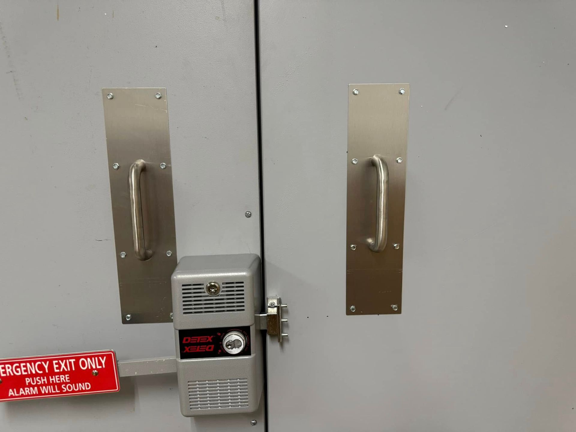 Gray double doors with metal handles and a security system; red