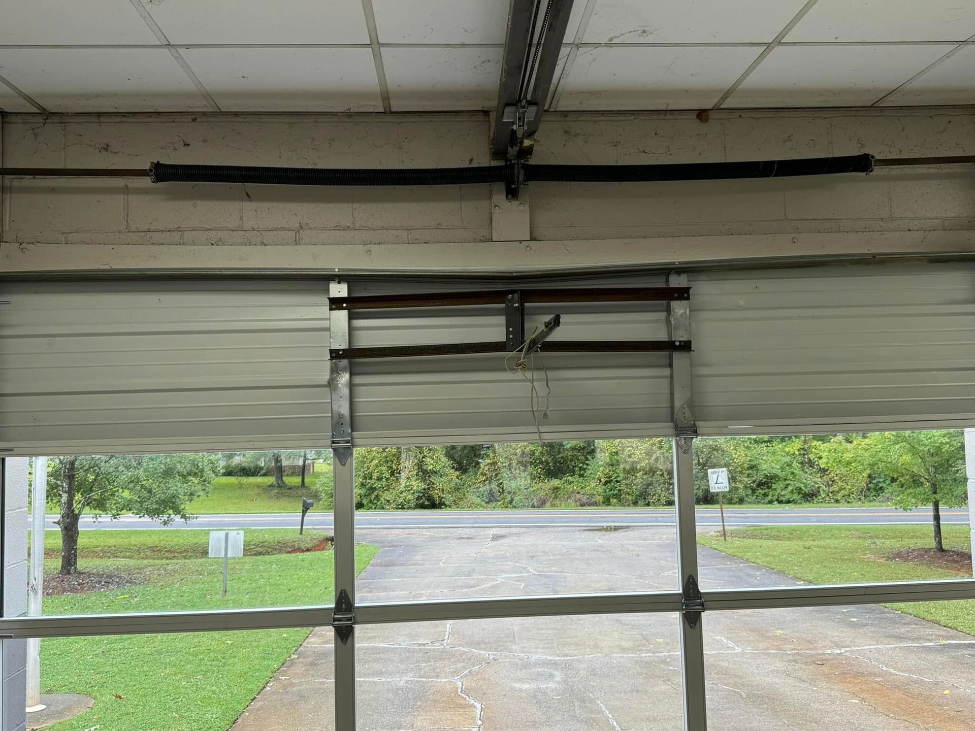 Open garage door showing a broken spring, with the driveway and yard visible outside.