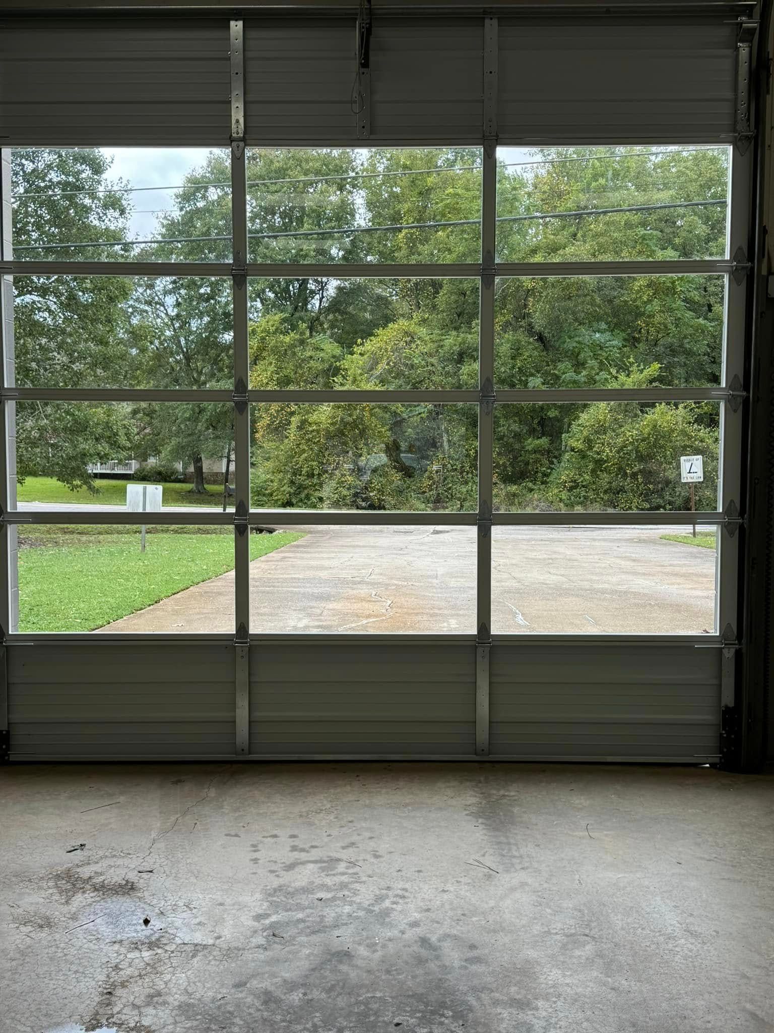 Garage door with glass panels open to a driveway and green trees outside.