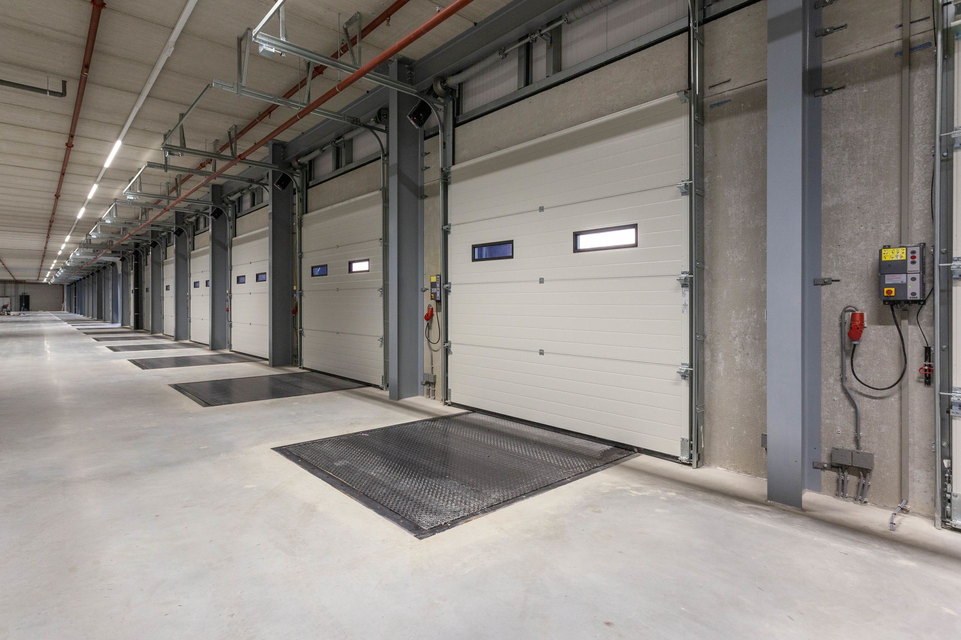 Loading dock with multiple closed garage doors and levelers, inside a warehouse.