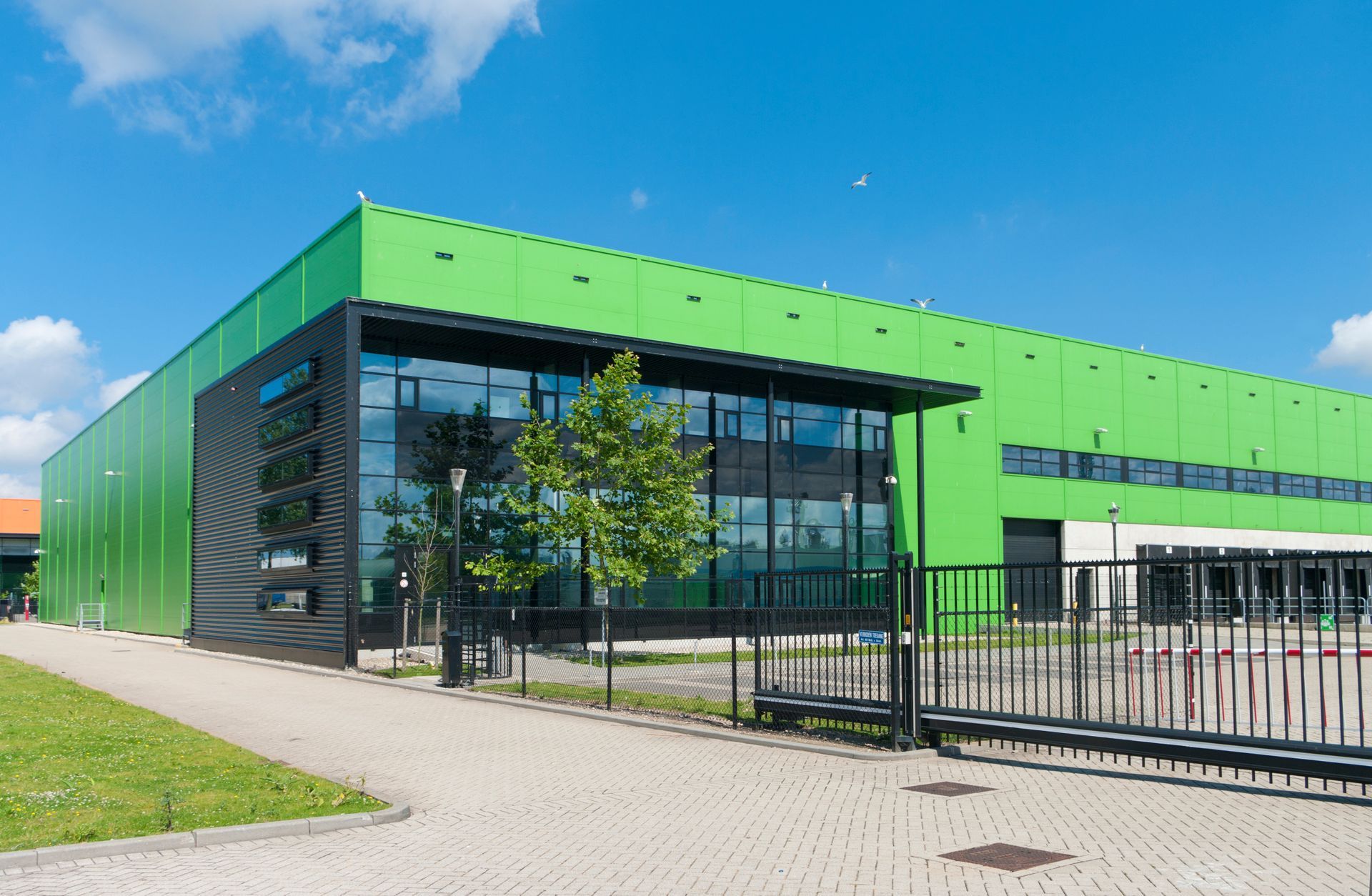 Green and black industrial building with glass windows under a blue sky.