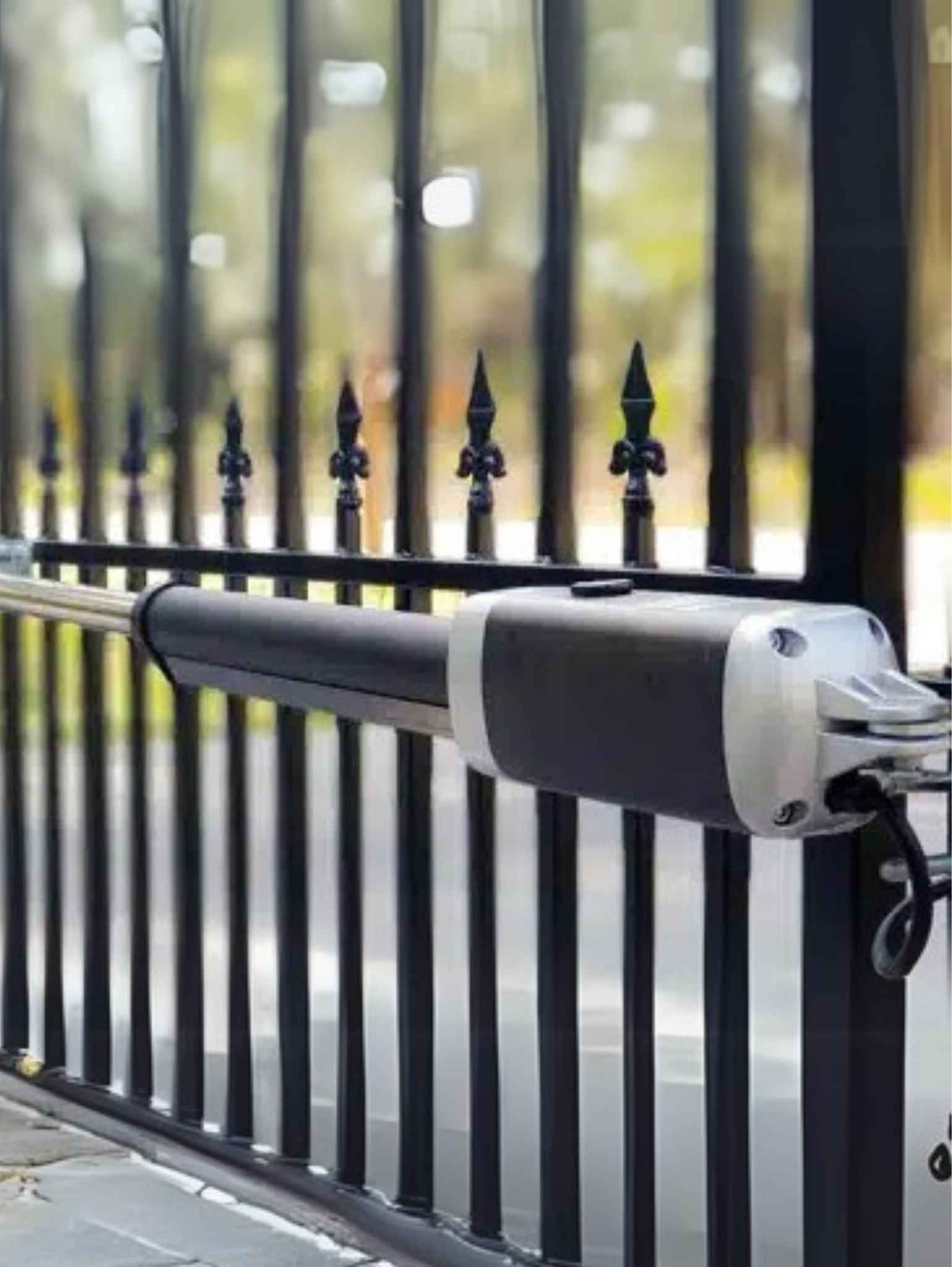 Automated gate arm attached to a black metal fence, in front of a blurred outdoor background.