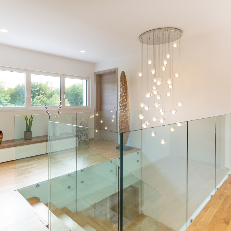 Modern home interior with glass railing staircase, wooden floors, and a hanging chandelier.