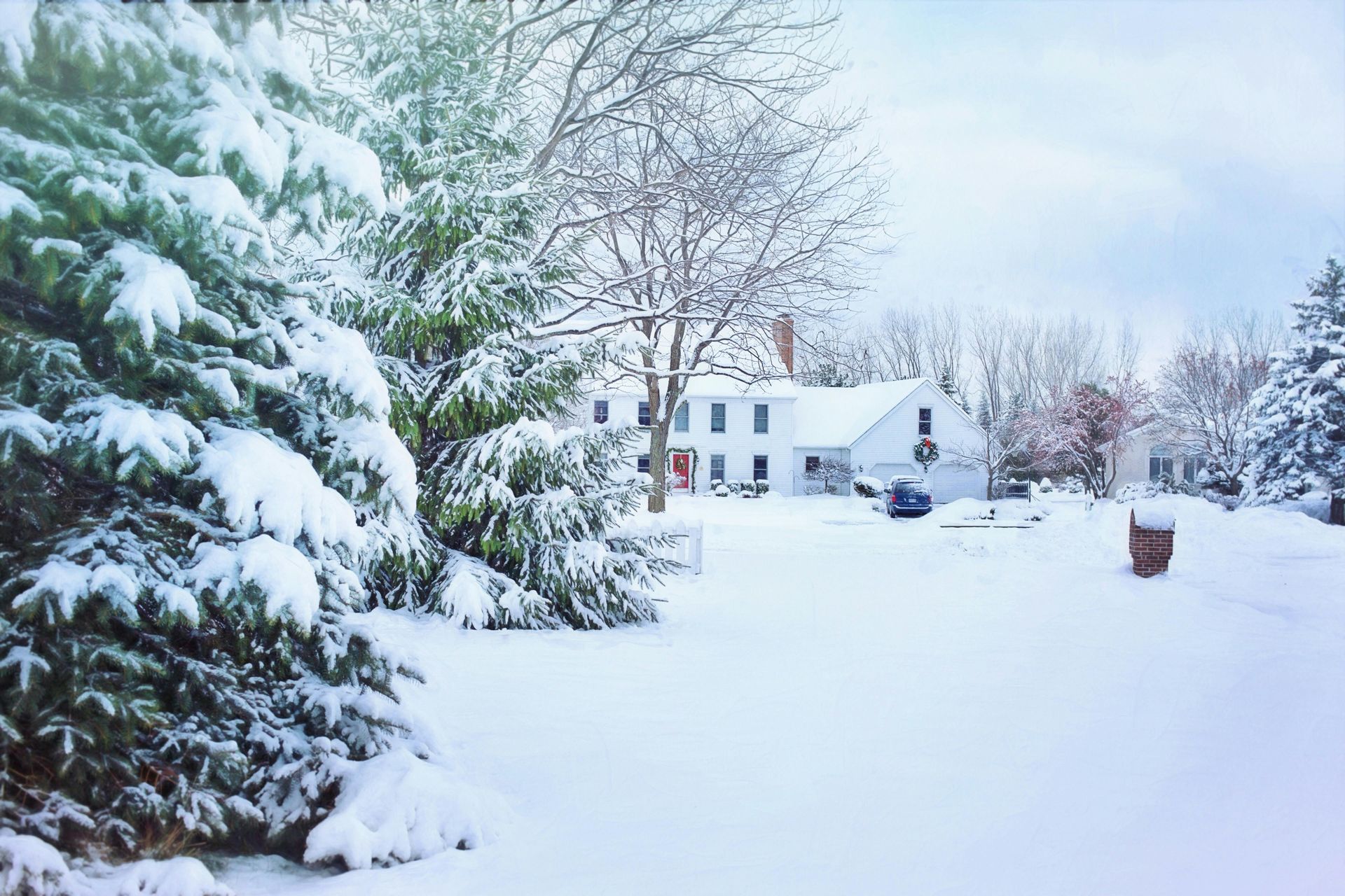 Snow-covered house and trees. White snow covers a yard and evergreens. Cloudy sky.