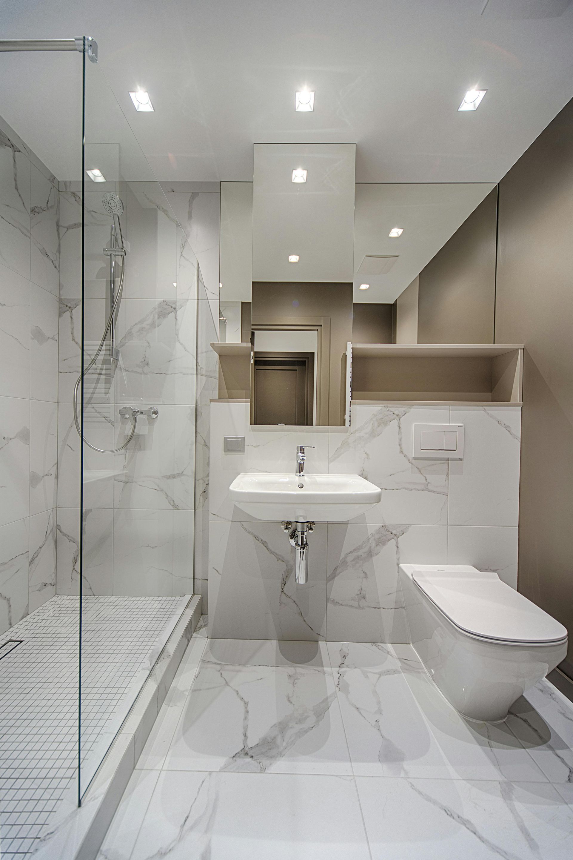 Modern bathroom with white marble tiling, glass shower, floating toilet, and a sink.