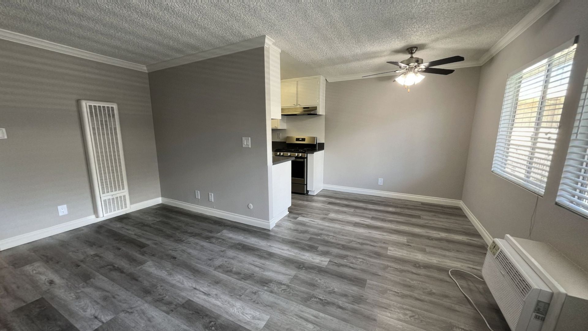 Gray-floored apartment interior with open kitchen and a ceiling fan.