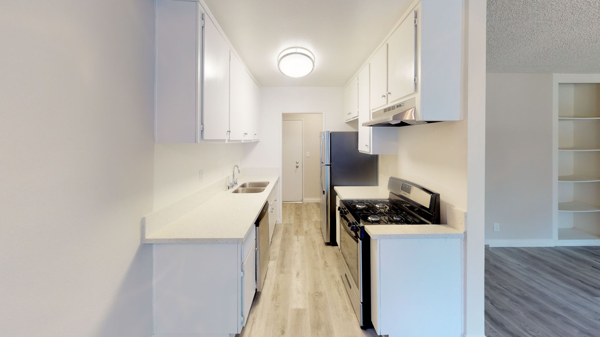 Narrow, bright kitchen with white cabinets, light countertops, and stainless steel appliances.