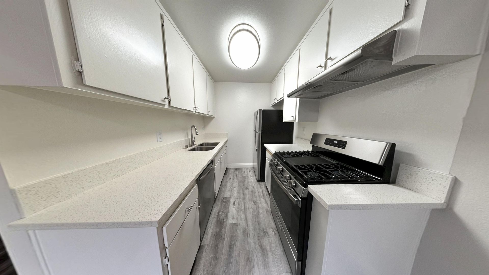 Narrow kitchen with white cabinets, light countertops, and black appliances.