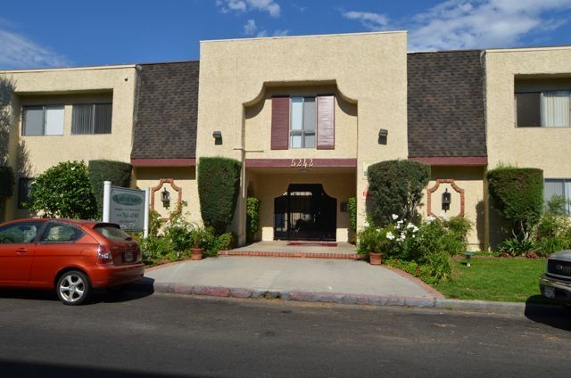 Apartment building with beige stucco facade, brown trim, and a red car parked out front.
