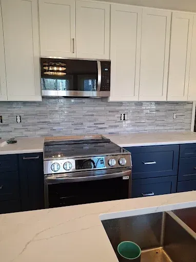 A kitchen with blue cabinets , a stove , a microwave , and a sink.