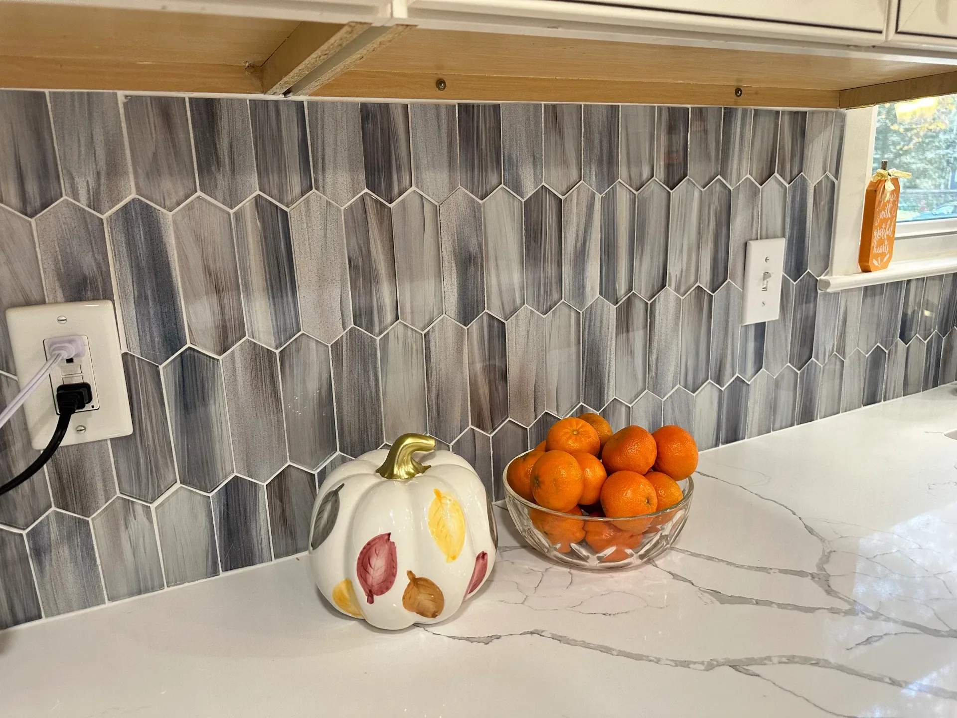 A kitchen counter with a bowl of oranges and a pumpkin on it.