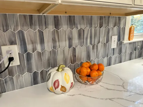 A kitchen counter with a bowl of oranges and a pumpkin on it.