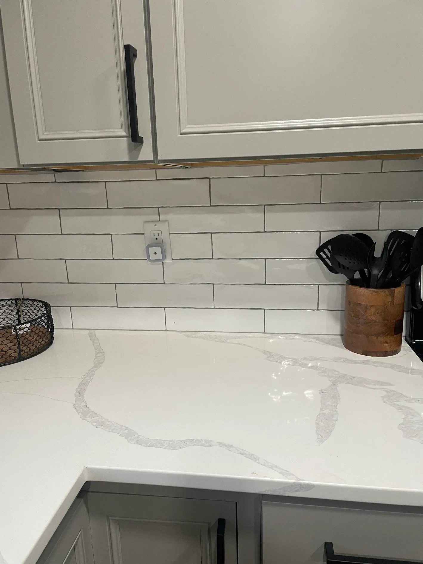 A kitchen counter with white cabinets and a wooden utensil holder.