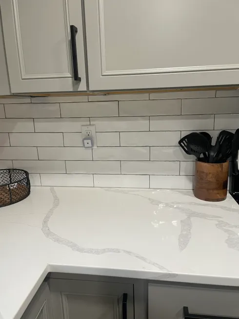 A kitchen counter with white cabinets and a wooden utensil holder.